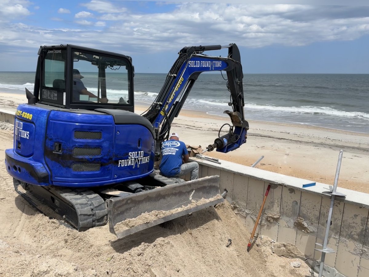 Solid Foundations crew and excavator repairing a seawall along a beach