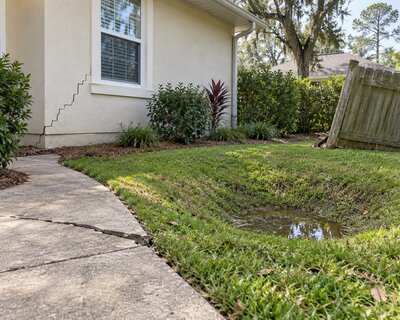 Stair-step crack along a home's exterior wall next to a yard where water is pooling after rain