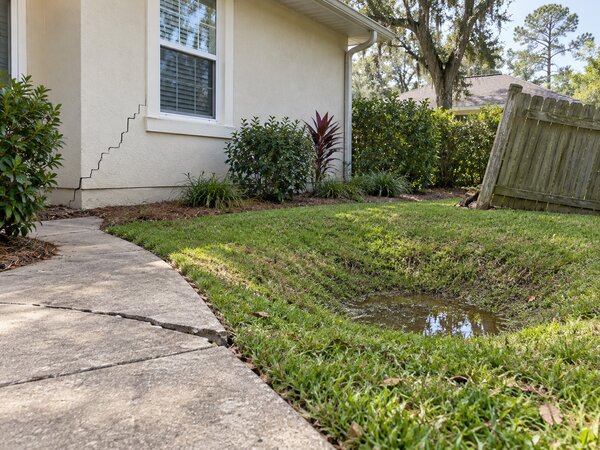 Stair-step crack along a home's exterior wall next to a yard where water is pooling after rain