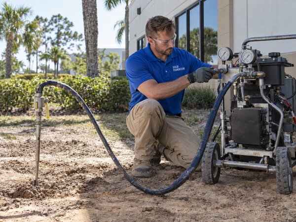 Solid Foundations technician operating polyurethane injection equipment connected to a soil stabilization port
