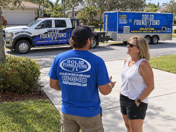 Solid Foundations technician talking with a homeowner beside the company truck and trailer